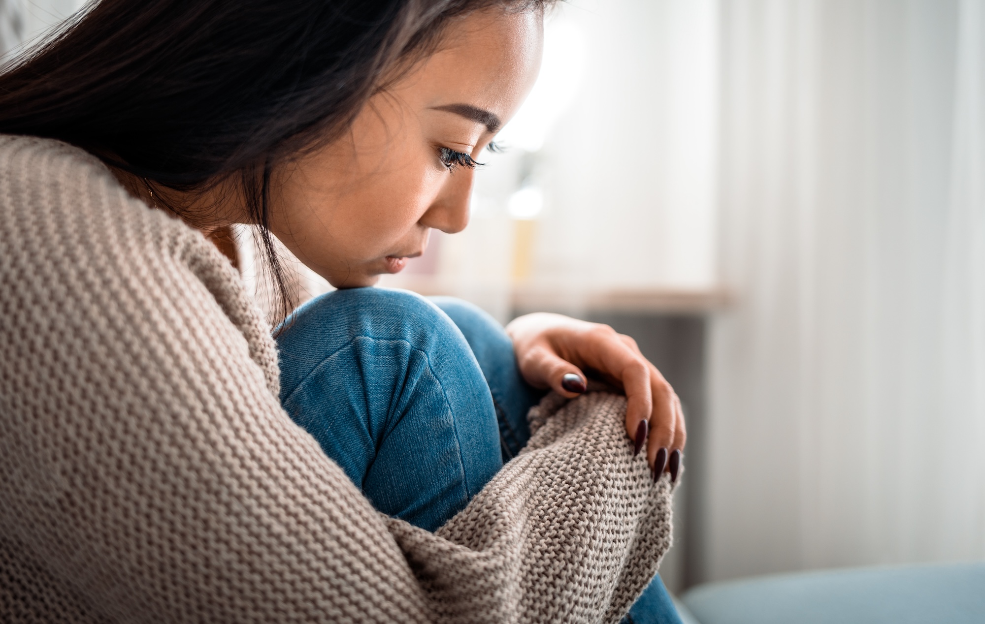 Young woman sitting with her knees up to her chest upset.
